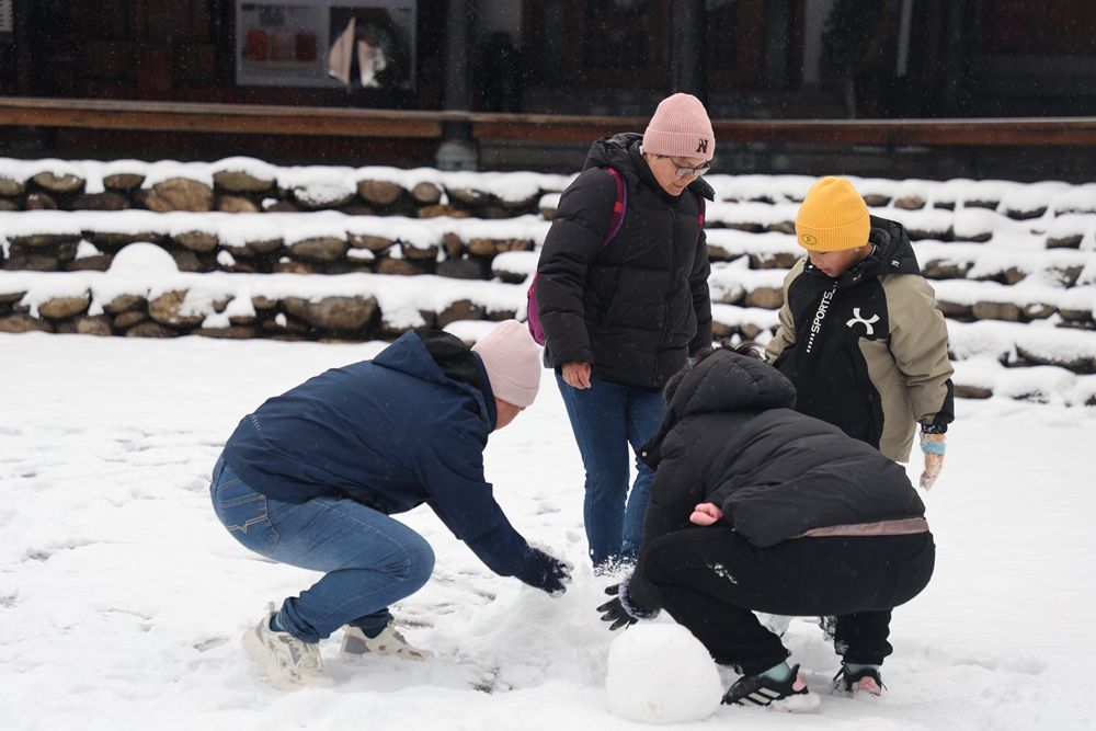 贵州雷山西江千户苗寨迎来降雪  冬日雪景如画_fororder_1月22日，贵州省雷山县西江千户苗寨迎来2024年第一场降雪。图为游客在蹲雪人。