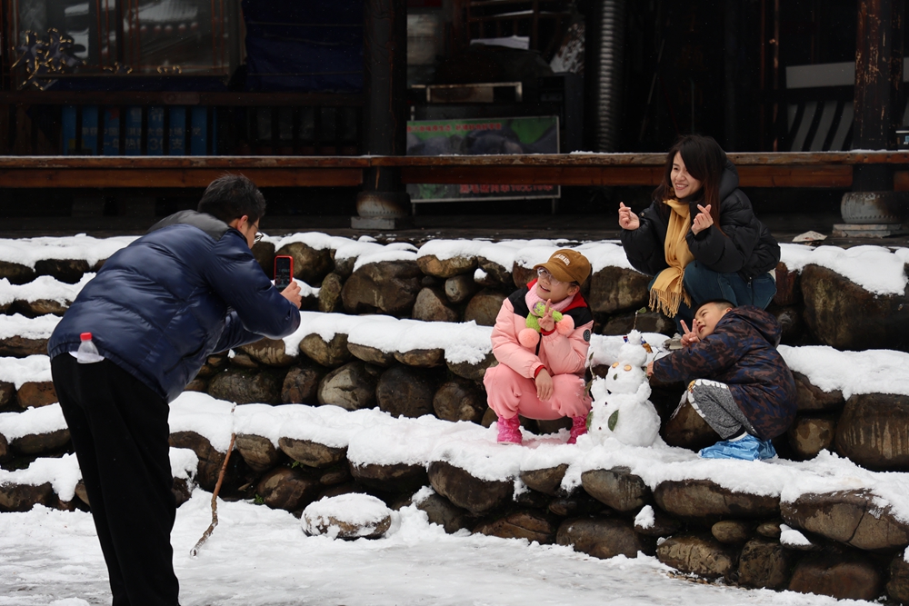 贵州雷山西江千户苗寨迎来降雪  冬日雪景如画_fororder_1月22日，贵州省雷山县西江千户苗寨迎来2024年第一场降雪。图为游客在合影留念。